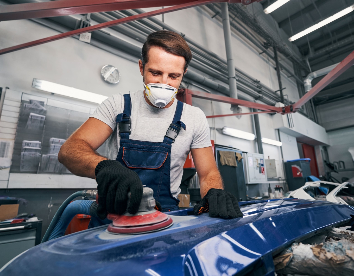 A worker sands down part of a car in an autobody shop.