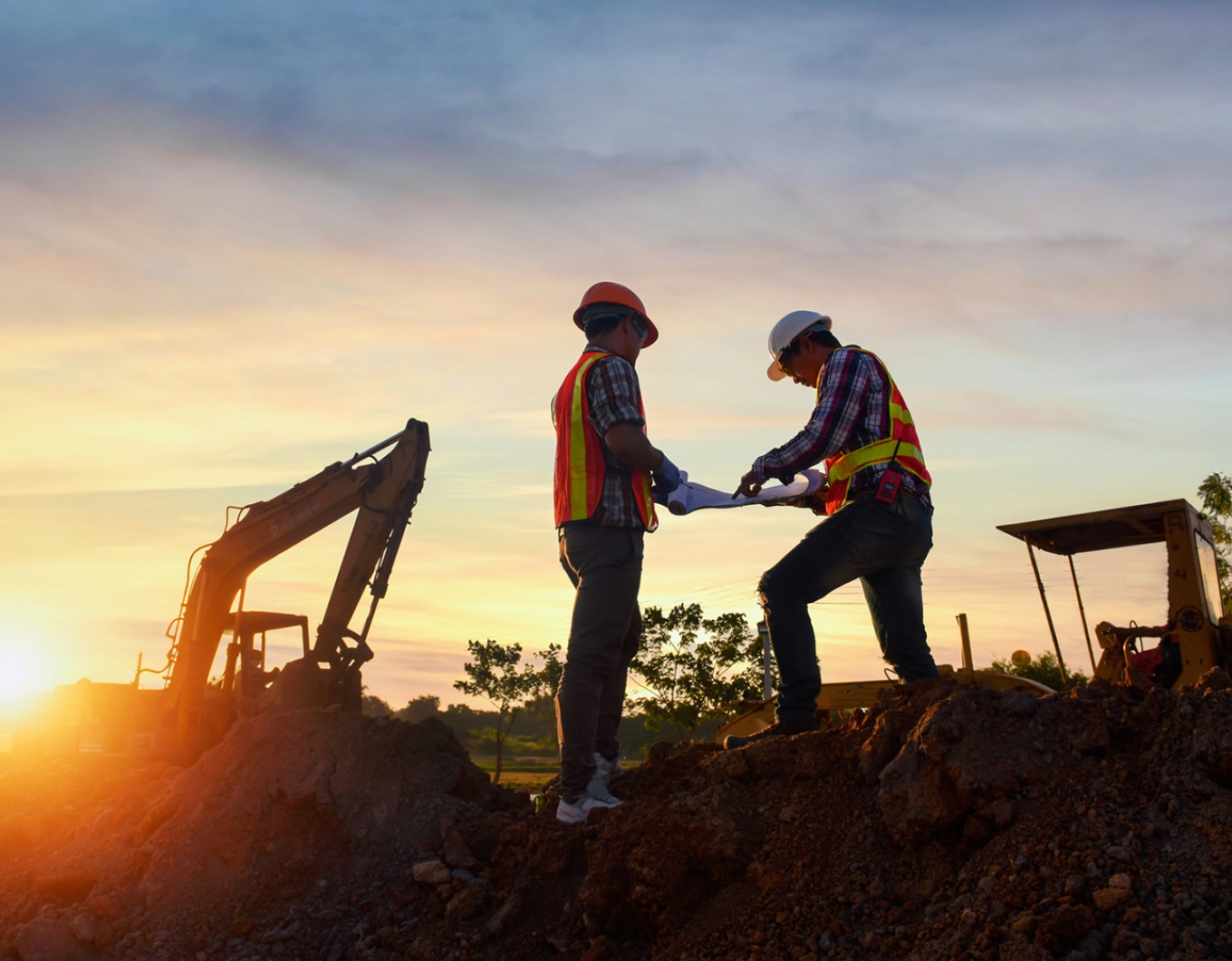 Two men in safety gear talk on a construction site.