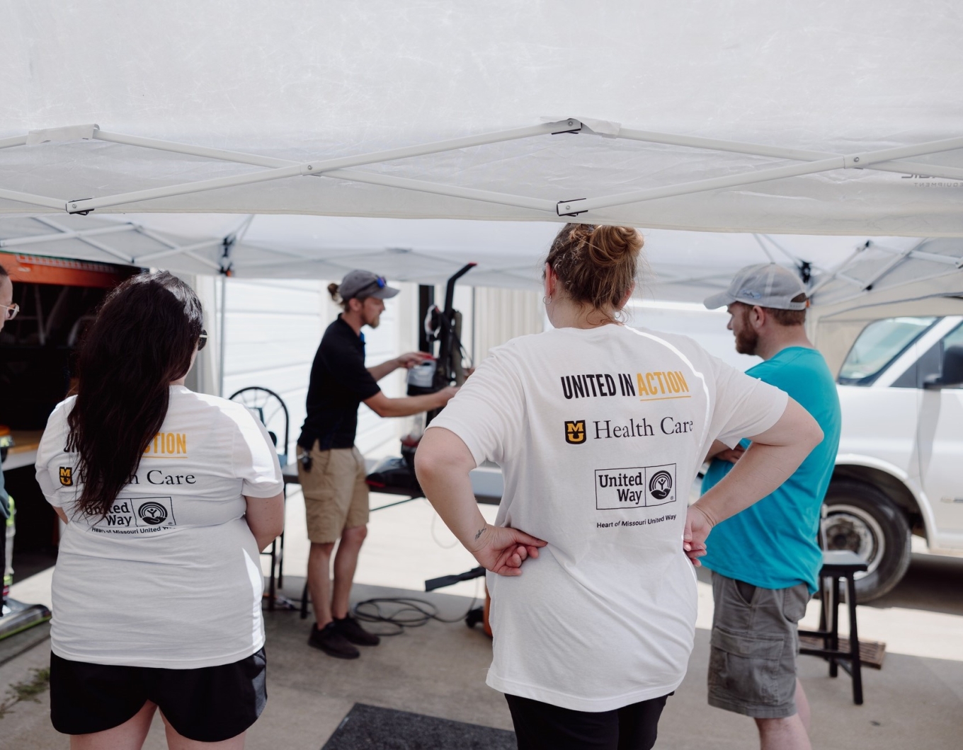 Four teammates watch a demo to repair a vacuum at United Way Week of Action.