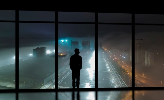 Man looks out of window at a storm.