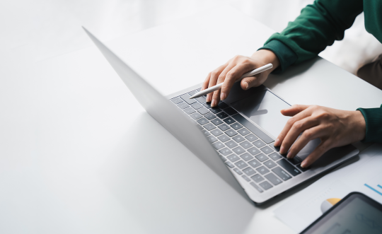 Two hands typing on a sliver laptop. 