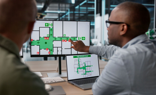 Two professionals look at fire escape routes on a computer screen.