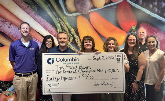 A group of eight people representing the Food Bank and Columbia Insurance pose with a large check.