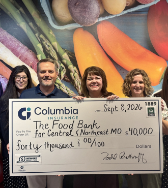 A group of eight people representing the Food Bank and Columbia Insurance pose with a large check.